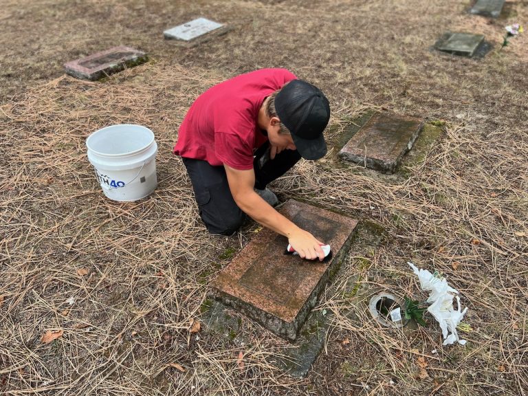 A volunteer scrubbing a flat grave marker