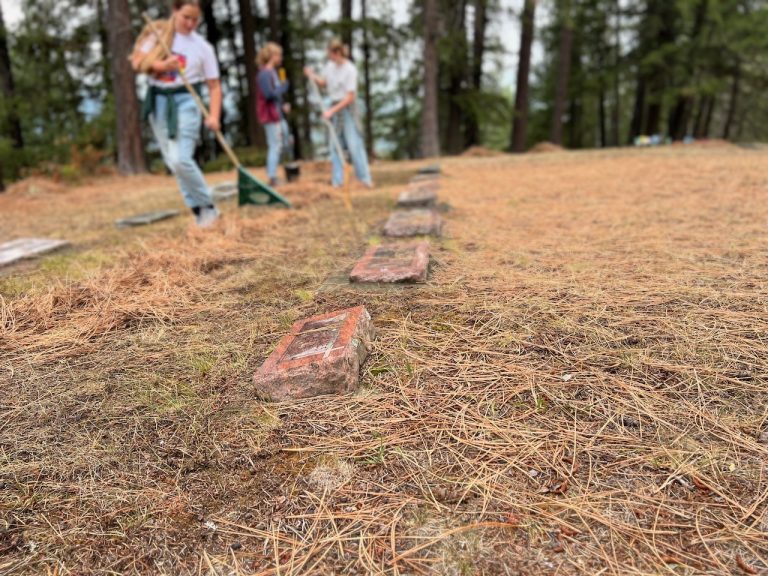 Volunteers clearing pine needles from grave markers